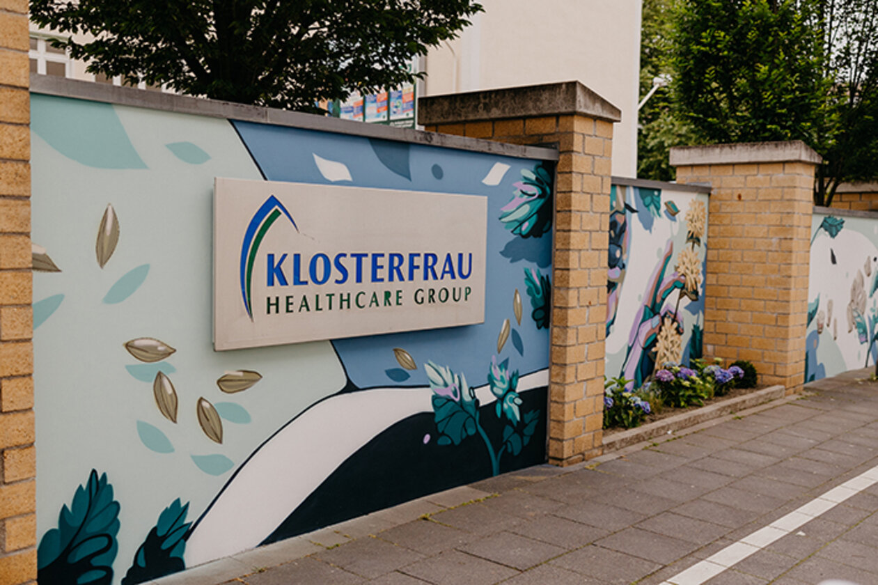 Mauer mit Klosterfrau-Logo und einem Street-Art-Gemälde, das Kräuter als Ausgangsprodukte für den bekannten Melissengeist zeigt.