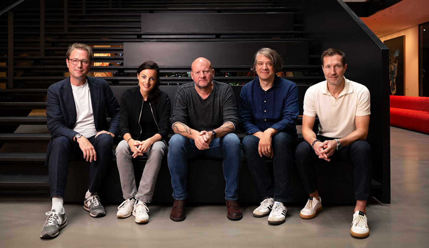 Eine Frau uns vier Männer sitzen nebeneinander auf einer Treppenstufe