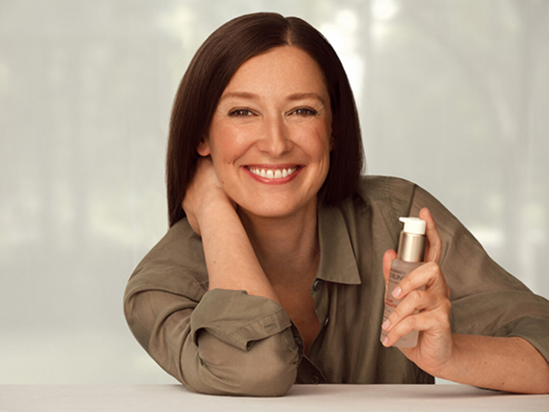 Schauspielerin Alexandra Maria Lara lächelt in die Kamera. In der Hand hält sie einen Flakon der Marke "Annemarie Börlind".