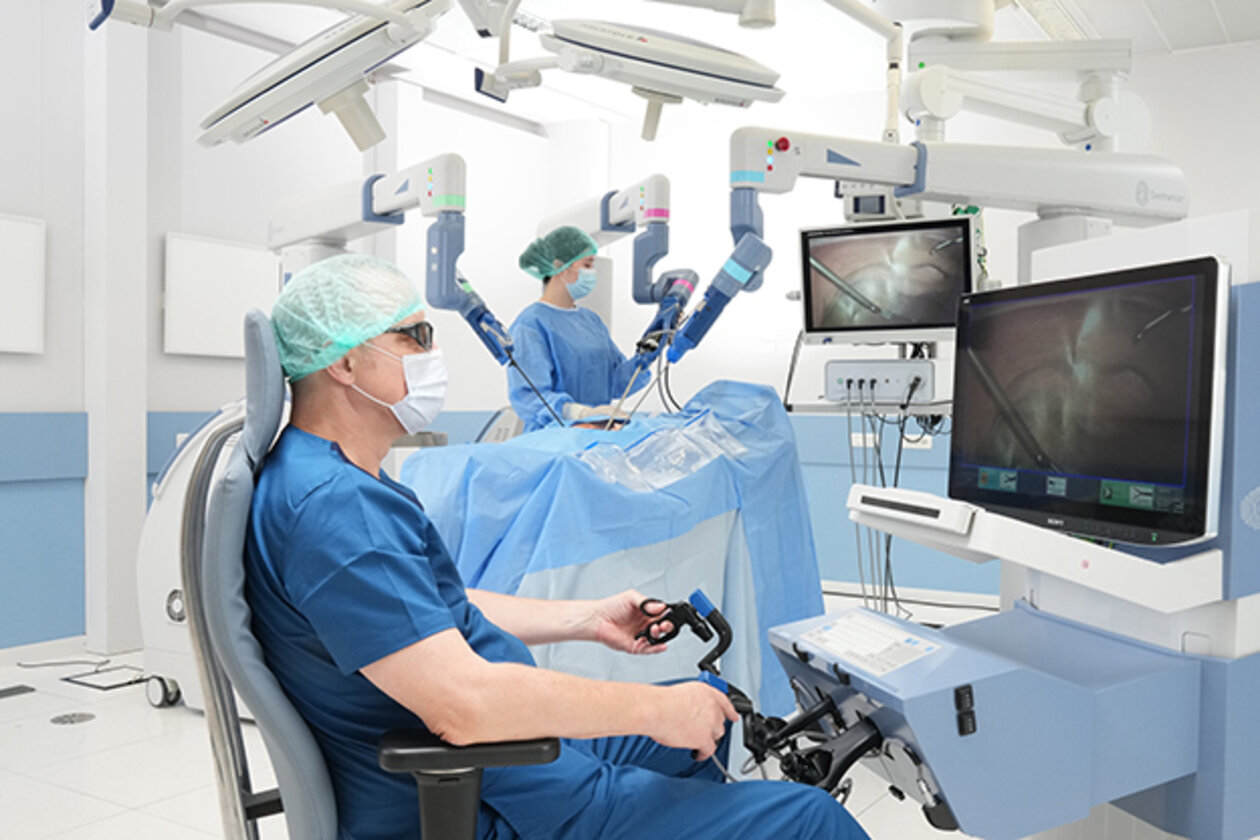Ein Chirug sitzt vor einem Bildschirm und operiert einen Patienten mithilfe eines Roboters.