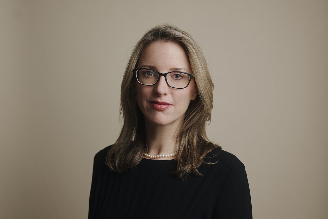 Eine Frau mit dunkelblonden schulterlangen Haaren und brauner Hornbrille lächelt dezent in die Kamera